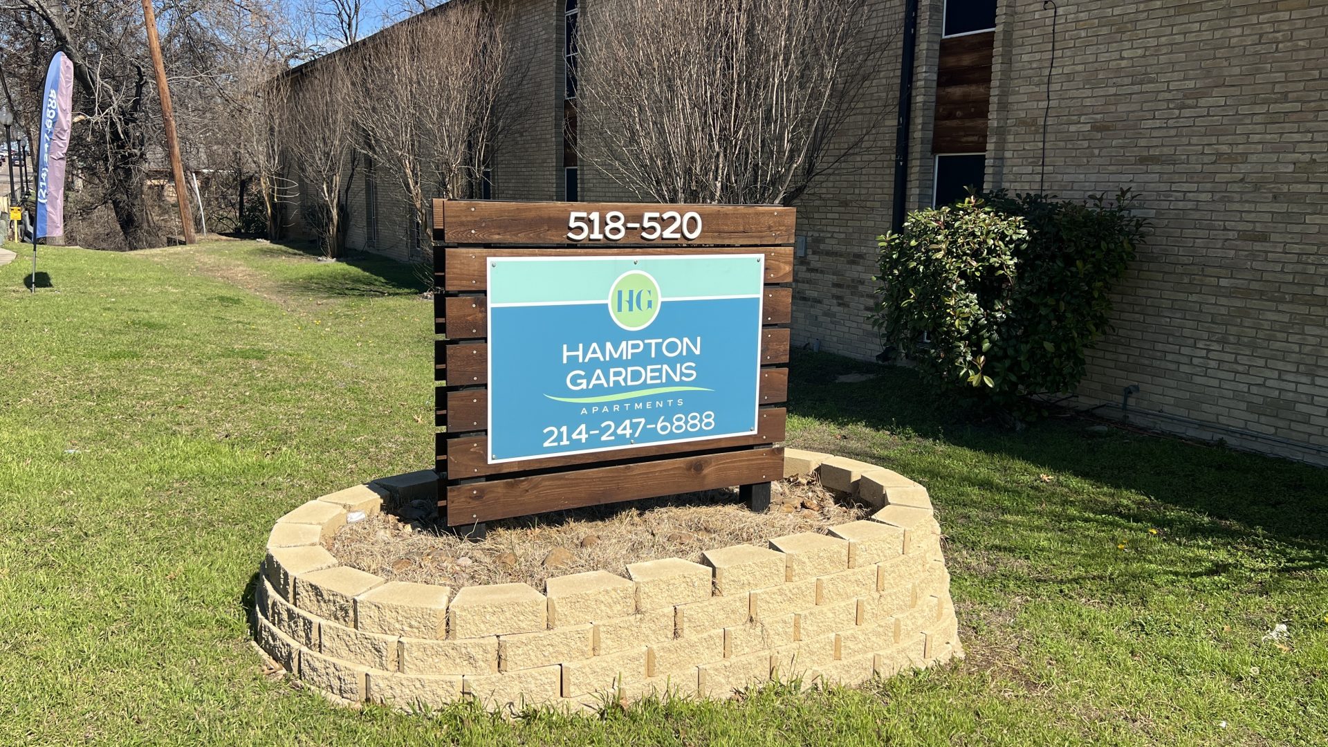 a sign for an apartment in front of a grassy area at The Hampton Gardens